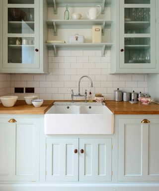 a blue green shade of blue kitchen with wood countertops, metro tile backsplash and glazed units, butler sink,