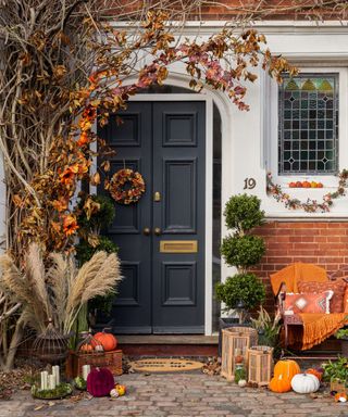 A fall front porch with pumpkins and dried flowers around it and a house with a dark blue door and white walls