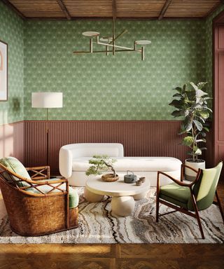 A living room with green wallpaper with brown paneling, a white couch, a woven chair, a green chair, and a wooden flooring with a woven rug on it