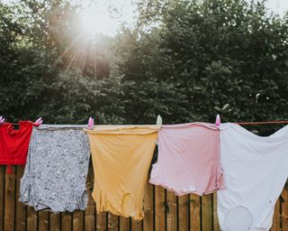 Various colours and sizes of clothing hanging in a row on a washing line outside, attached to the line with plastic clothes pegs