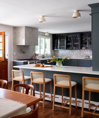 blue gray kitchen with white marble countertops, bar stools, pearlescent wall tiles, brass hardware and facceut, cherry wood style floor, table,