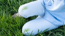 Close up of lady sitting in long grass, with dirty grass stains on light blue denim jeans - for article on how to remove grass stains