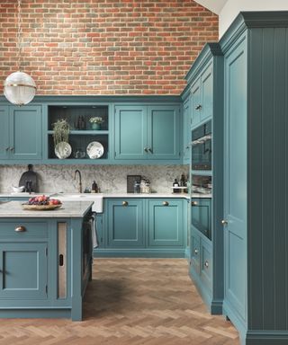 teal blue kitchen with marble countertops, herringbone floor, exposed brick wall, marble backsplash, brass tap and hardware,