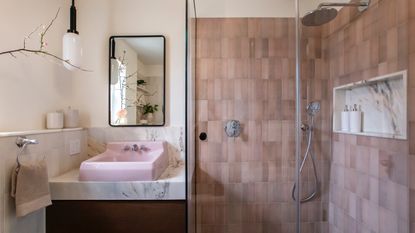 Pink bathroom with pink sink, marble backsplash, pink tiled shower, mirror, white pendant lights