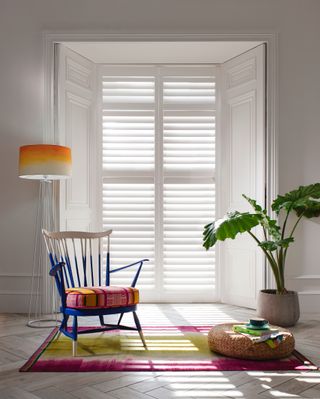 White shutters in bright room with colorful chair and houseplant