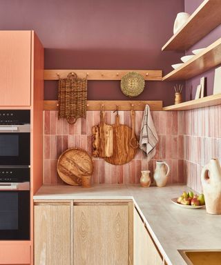 A kitchen with purple walls, light pink tiles, wooden shelves, and a white kitchen countertop