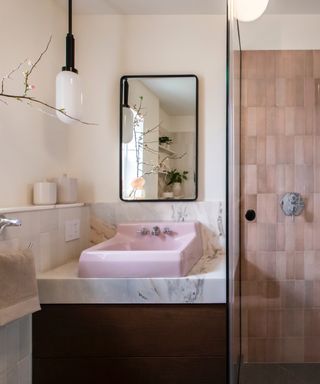 pink bathroom with pink sink, marble backsplash, pink tiled shower, mirror, white pendant lights