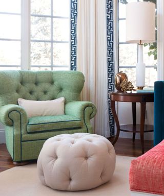 A living room with a pistachio green chair, a white tufted storage ottoman, and a large window behind the seats