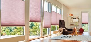 Pink blinds over patio doors in a living room with black chair by duette